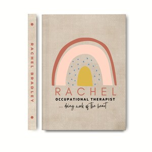 May include: A tan linen notebook with a rainbow design in pink, red, and yellow. The notebook has the name "Rachel" and the text "Occupational Therapist... doing work of the heart" printed on it.