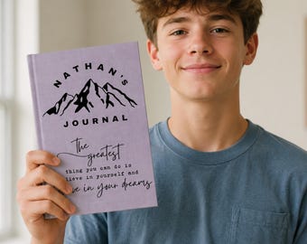 May include: A light purple hardcover journal featuring a black mountain graphic and the text NATHAN'S JOURNAL. Below the graphic, the text reads The greatest thing you can do is believe in yourself and live in your dreams in black script and print.