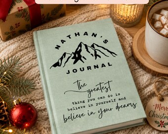 May include: A sage green hardcover journal featuring a black mountain graphic and the text "NATHAN'S JOURNAL" followed by the quote "The greatest thing you can do is believe in yourself and believe in your dreams" printed in black ink on the front cover.