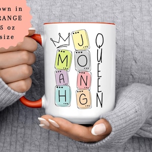 May include: White ceramic mug with a red interior and handle, featuring the words "MOM" and "QUEEN" spelled out with colorful letter tiles. A crown graphic is above the word "MOM". The mug is 15 oz in size.