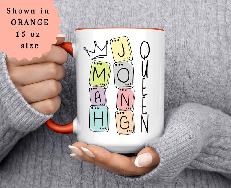 May include: White ceramic mug with a red interior and handle, featuring the words "MOM" and "QUEEN" spelled out with colorful letter tiles. A crown graphic is above the word "MOM". The mug is 15 oz in size.