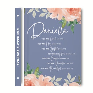 May include: A blue journal with a floral watercolour design featuring peach-coloured roses and green leaves. The cover displays the name Daniella and text including You are Loved, His, Gifted, an Heir, Chosen, Valuable, and Beautiful with scripture.