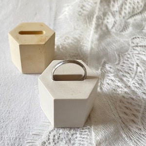 Peut inclure: Deux supports de bague hexagonaux blancs. Un support contient une bague argentée. Les deux supports ont une surface lisse et texturée.