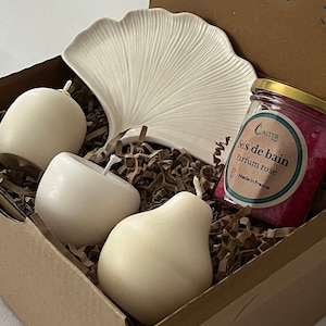 Peut inclure: Une boîte cadeau remplie de produits de bain, dont un plat en céramique blanche en forme de feuille, trois bougies blanches et un pot de sels de bain roses étiqueté "Sels de bain parfum rose" avec la marque "ALTER" et "Fabriqué en France".