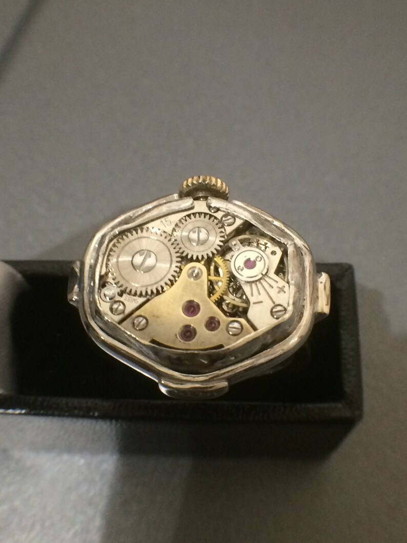 May include: A silver and gold watch with a unique octagonal shape. The watch is open, revealing the intricate inner workings of the mechanism.