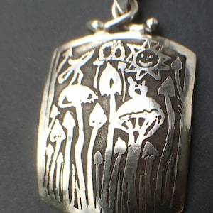 Puede incluir: Un colgante de plata con un diseño detallado de setas y un sol con una cara sonriente. El colgante está en una cadena de plata.