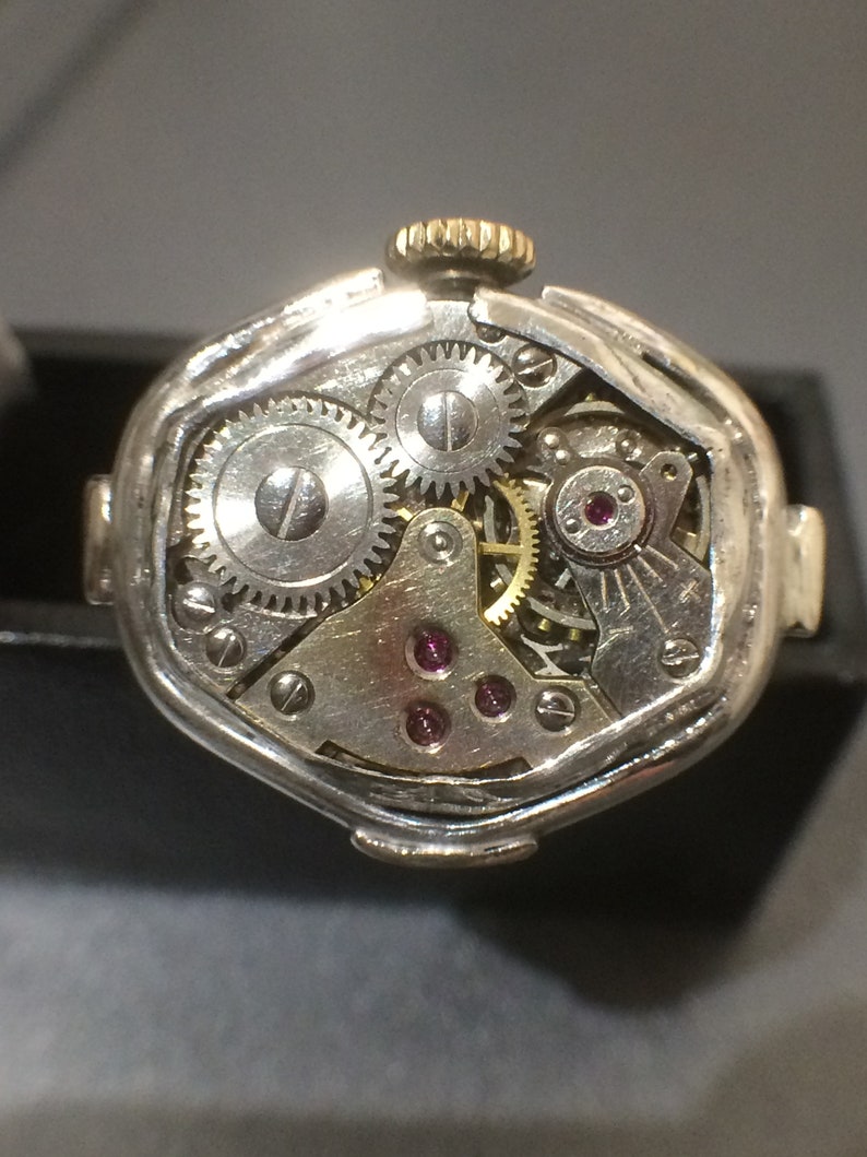 May include: A silver watch with a round face and a gold crown. The watch is open and the inner workings are visible. The watch has a silver band and a silver case.