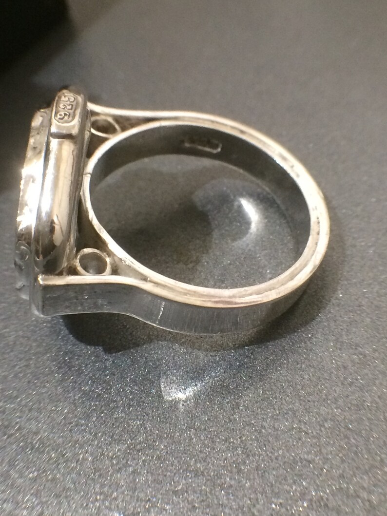 May include: A silver ring with a detailed design and the number "925" engraved on the side.