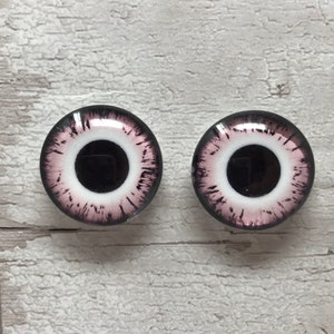 May include: Two round glass eyes with a black pupil, white iris, and pink and black details. The eyes are for crafts and doll making.