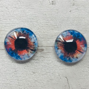 May include: Two round glass eyes with a blue, orange and white swirl pattern. The iris is black and the pupil is a dark grey.