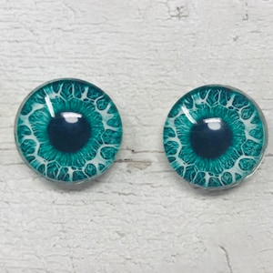 Puede incluir: Dos ojos redondos de vidrio con un iris azul verdoso y una esclerótica blanca. Los ojos tienen un patrón detallado de venas y una pupila azul oscura.