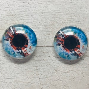 May include: Two glass eyes with blue, white and orange irises and black pupils. The eyes are round and have a glossy finish.