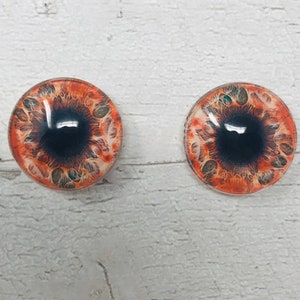 May include: Two round orange and black glass eyes with a detailed design. The eyes are set against a white background.