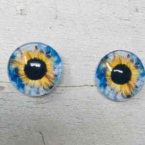 May include: Two round glass eyes with a blue and yellow sunflower design. The iris is black and the pupil is a dark circle.