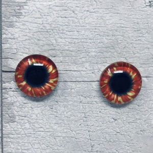 May include: A pair of red and gold glass eyes with black pupils. The eyes are round and have a realistic look.