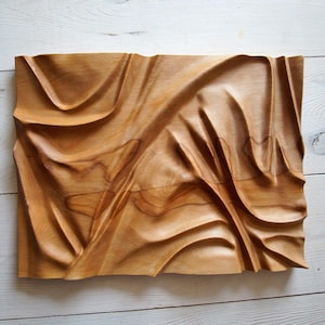May include: A wooden wall sculpture with a flowing, abstract design. The sculpture is carved from light brown wood and has a smooth, polished finish.