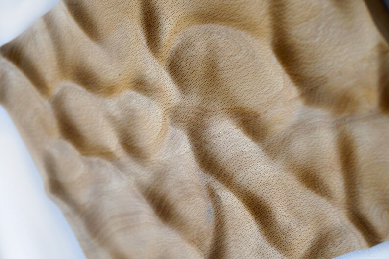 Puede incluir: Primer plano de una superficie de madera texturizada de color marr&oacute;n claro con un patr&oacute;n ondulado. La veta de la madera es visible y la superficie tiene un aspecto suave y t&aacute;ctil. El efecto general es natural y org&aacute;nico.