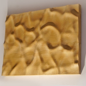 Puede incluir: Una pieza de arte mural rectangular de madera con una superficie texturizada. La madera es de color marr&oacute;n claro con acentos marr&oacute;n oscuro, creando un aspecto natural y org&aacute;nico. La superficie tiene un patr&oacute;n ondulado, agregando profundidad.
