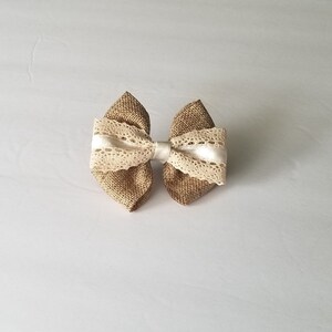 以下が含まれることがあります： 白いレースと白いサテンリボンの中央に、茶色の麻のボウタイが付いたもの