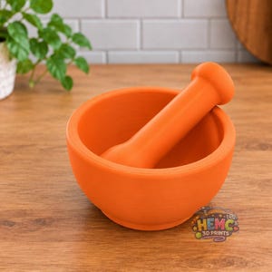Peut inclure: Un mortier et un pilon orange vif avec une finition mate et lisse. Le bol est circulaire avec une large ouverture, et le pilon est cylindrique avec une extrémité arrondie. Un petit logo avec le texte HEMC 3D PRINTS est visible près de la base.