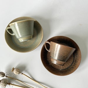 以下が含まれることがあります： セラミック製のティーカップとソーサー2つ。1つのカップとソーサーは茶色の釉薬がかかった緑色、もう1つは黒色の釉薬がかかった茶色です。