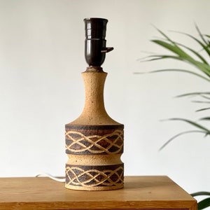 Puede incluir: Una lámpara de mesa de cerámica con una base marrón y beige con un diseño tejido. La lámpara tiene un casquillo marrón y un cable blanco.