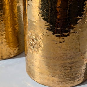 May include: Two gold metal table lamps with a hammered finish and a decorative floral design. The lamps have a distressed look.