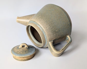 Może przedstawiać: Ceramiczny czajnik z niebiesko-brązową glazurą w kropki. Czajnik ma pokrywkę z małym uchwytem. Czajnik stoi na białym tle.