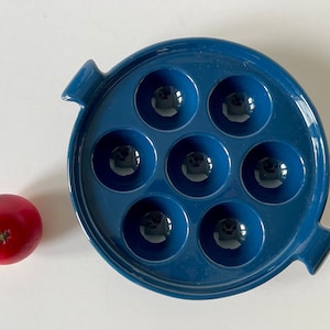 May include: A blue ceramic baking dish with eight round indentations for making individual portions of food. The dish has two handles on the sides.