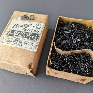 May include: A box of black metal mantle hooks and eyes, labelled "Newey's Pelican Mantle Hooks & Eyes, 3 Gross No. 303, Made in England, Black".