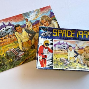 May include: A vintage "Space 1999" jigsaw puzzle, partly assembled, with its box. The puzzle depicts a sci-fi scene with astronauts and spacecraft. The box displays the text "SPACE 1999 JIGSAW PUZZLE" and an astronaut in red.