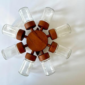 Puede incluir: Un estante de especias de madera con ocho frascos de vidrio. El estante está hecho de madera oscura y tiene una base circular. Los frascos son de vidrio transparente y están dispuestos en un círculo alrededor de la base.