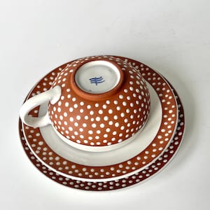 May include: A brown teacup and saucer set with white polka dots. The bottom of the teacup has a blue mark with a symbol.