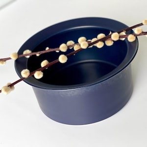 Könnte beinhalten: Eine dunkelblaue Keramikschale mit breitem Rand, gefüllt mit Zweigen von Weidenkätzchen mit flauschigen weißen Knospen.