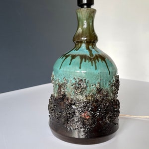 May include: A ceramic table lamp with a textured, dark brown and green glaze. The lamp has a wide base and a narrow neck.