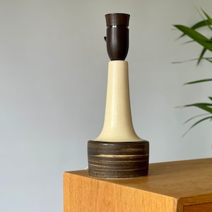 May include: A ceramic table lamp with a brown and cream glaze. The lamp has a wide base and a narrow neck. The lampshade is not included.
