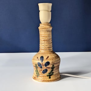May include: A ceramic table lamp with a brown and beige base, decorated with blue and green floral designs. The lamp has a white cord and a white lightbulb.
