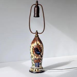 May include: A ceramic table lamp with a brown, yellow, and blue floral design featuring a bird. The lamp has a metal base and a metal shade.