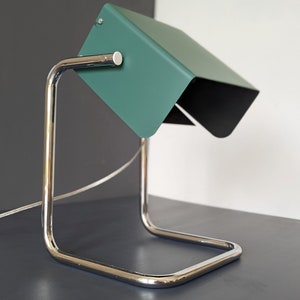 May include: A green metal desk lamp with a chrome base and a flexible arm. The lamp is on a grey surface.