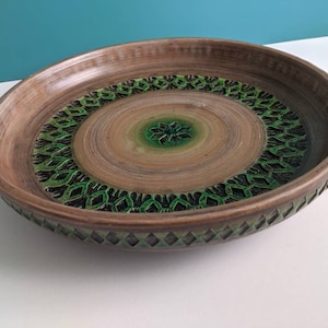 Op de afbeelding: Een grote, ronde, bruine keramische serveerschaal met een geometrisch ontwerp in groen en zwart. De schaal heeft een verhoogde rand en een licht concave bodem.