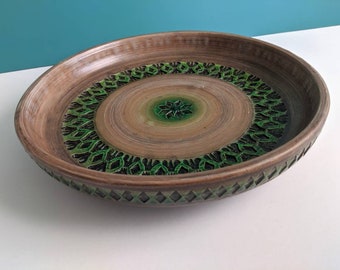 May include: A large, round, brown ceramic serving dish with a green and black geometric design. The dish has a raised rim and a slightly concave center.