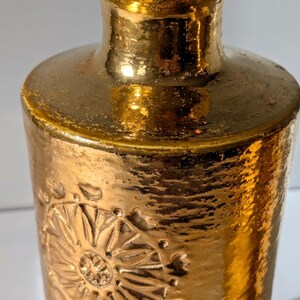 May include: A pair of gold ceramic vases with a textured surface and embossed floral designs. The vases have a slightly flared top and a rounded bottom.