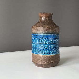 May include: A ceramic vase with a textured brown top and base, and a band of blue, patterned tiles around the middle. The vase has a narrow neck and a cylindrical body. The vase is approximately 8 inches tall.