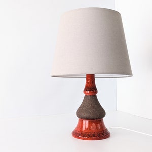 May include: A ceramic table lamp with a brown and orange base and a beige fabric lampshade.