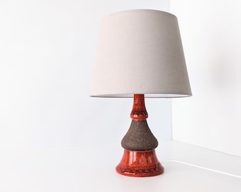 May include: A ceramic table lamp with a brown and orange base and a beige fabric lampshade.