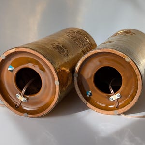 May include: Two brown ceramic table lamps with gold accents and a textured surface. The lamps have a round opening at the bottom for a cord.