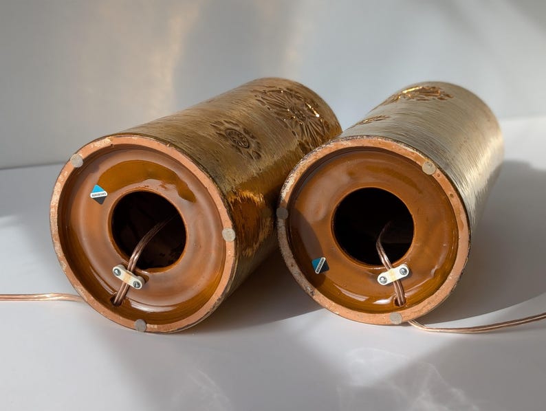 May include: Two brown ceramic table lamps with gold accents and a textured surface. The lamps have a round opening at the bottom for a cord.