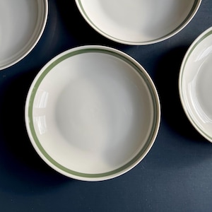 May include: Four white ceramic bowls with a green rim. The bowls are arranged in a semi-circle on a dark blue surface.