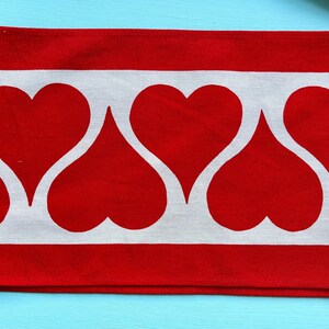 May include: Red and white fabric with a repeating pattern of white hearts on a red background.