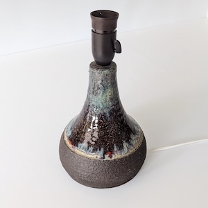 May include: A ceramic table lamp with a dark brown, blue, and green glaze. The lamp has a simple, rounded shape and a black metal socket.
